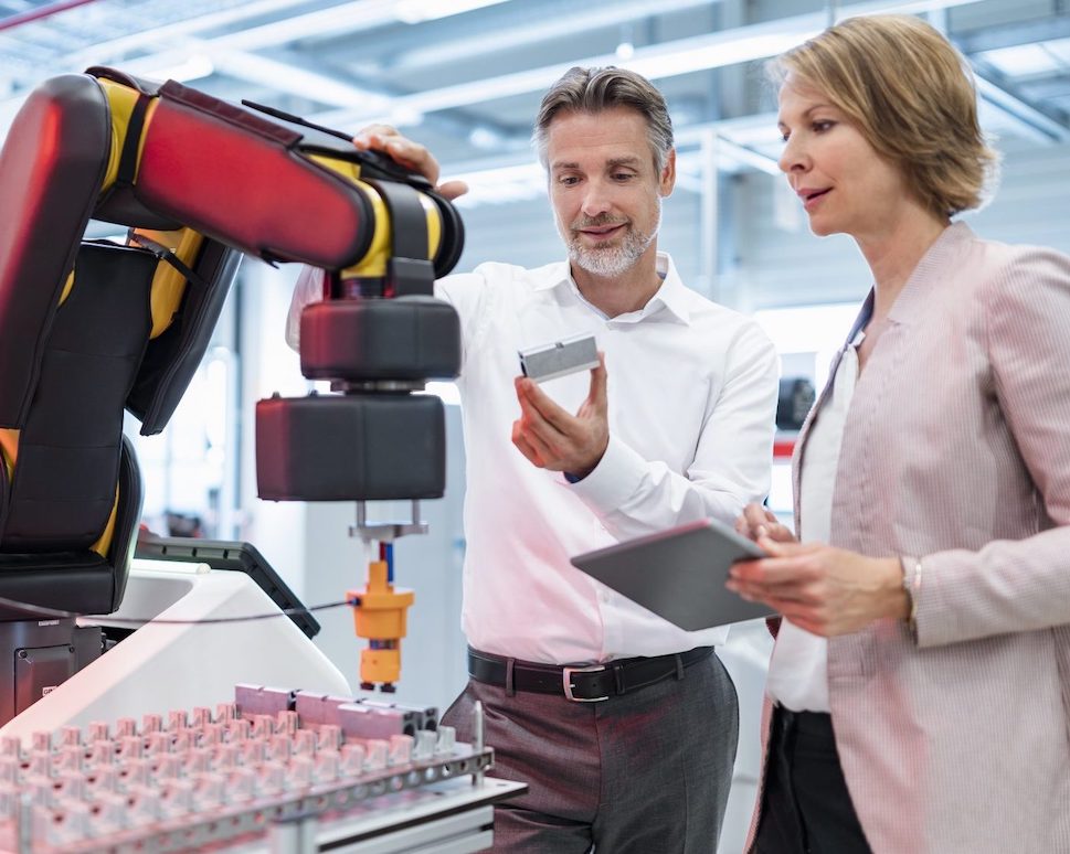 man and woman in a lab looking at a robotic arm
